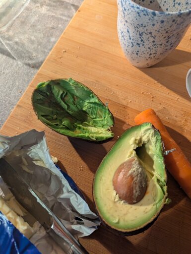 A photo of two halves of an avocado, at which someone has hacked away with a butter knife and a great deal of violence.
