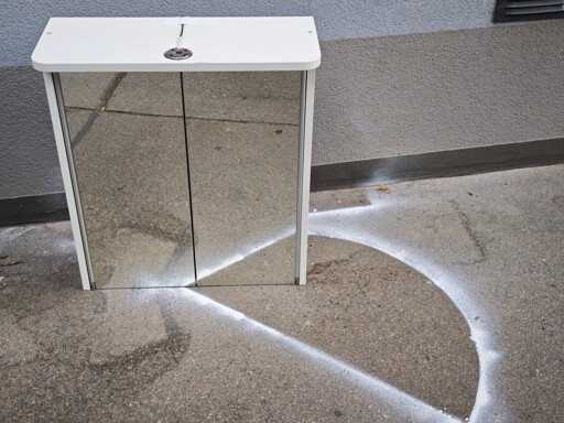 Mirrored Cabinet, left out in just the right spot to fit to a white, almost semicircular marking on the sidewalk. The mirrored image fits the existing figure, but the photographer was shit and botched it. 